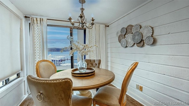 dining area featuring hardwood / wood-style flooring, a notable chandelier, wood walls, and a water view