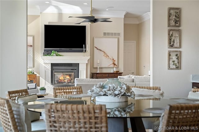 living area featuring visible vents, a glass covered fireplace, recessed lighting, ornamental molding, and a ceiling fan
