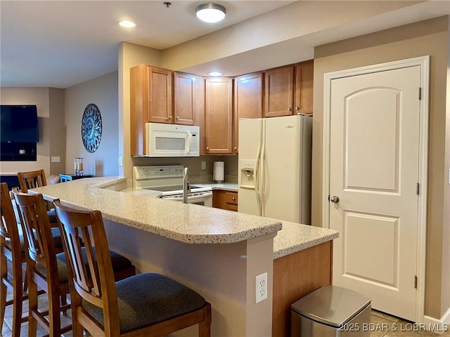 kitchen featuring light stone countertops, a kitchen bar, white appliances, and kitchen peninsula