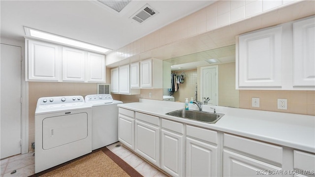 clothes washing area with sink, washer and clothes dryer, light tile patterned floors, and cabinets