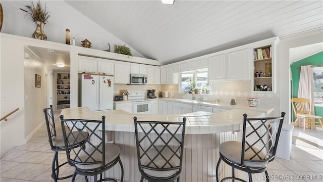 kitchen with white appliances, white cabinets, decorative backsplash, and a kitchen bar