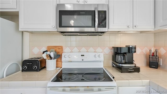 kitchen with white electric stove, tasteful backsplash, and white cabinetry