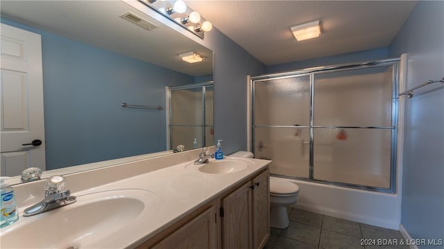 full bathroom featuring vanity, a textured ceiling, shower / bath combination with glass door, tile patterned flooring, and toilet