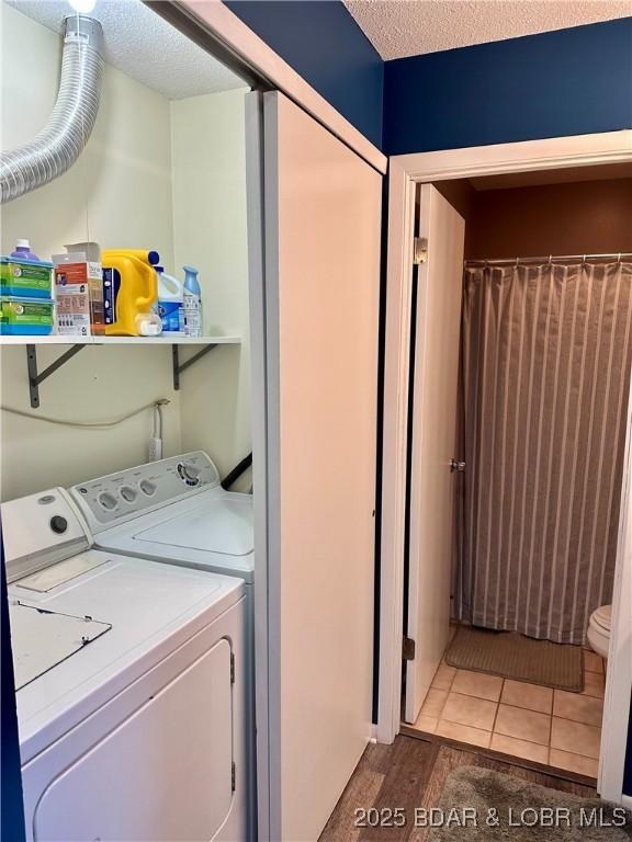 clothes washing area with independent washer and dryer, tile patterned flooring, and a textured ceiling