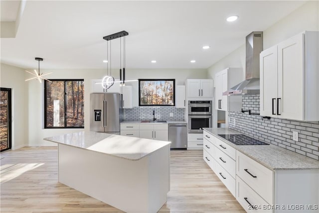 kitchen featuring pendant lighting, a center island, white cabinets, wall chimney exhaust hood, and appliances with stainless steel finishes