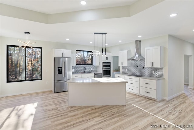 kitchen featuring white cabinets, a center island, wall chimney exhaust hood, and appliances with stainless steel finishes