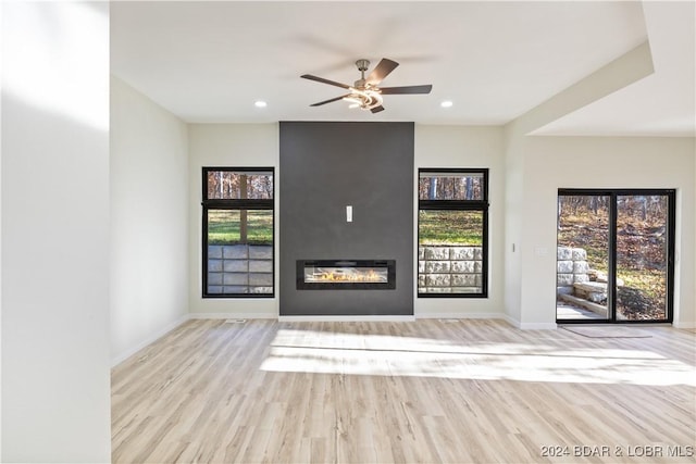 unfurnished living room with ceiling fan, a large fireplace, and light hardwood / wood-style floors