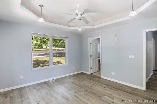 empty room with light wood-type flooring, a raised ceiling, and ceiling fan