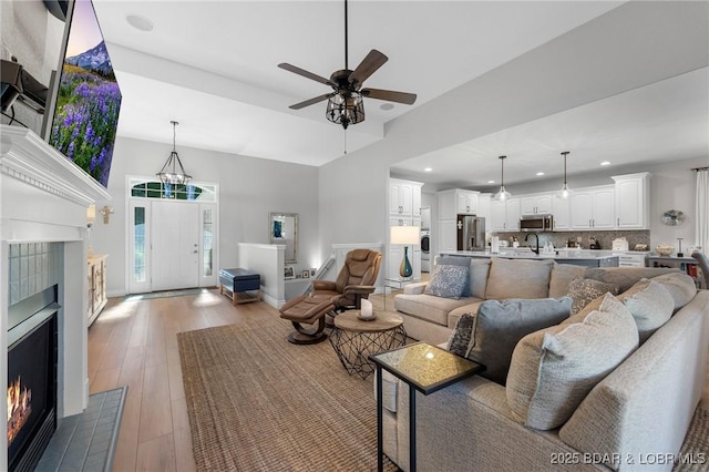 living room featuring a tiled fireplace, ceiling fan, sink, and wood-type flooring