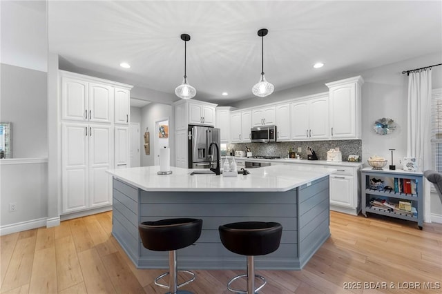 kitchen with white cabinets, a center island with sink, a breakfast bar area, and appliances with stainless steel finishes