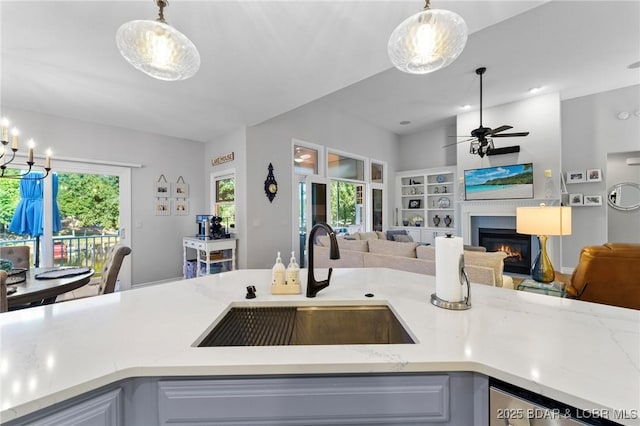 kitchen with light stone countertops, sink, ceiling fan, and hanging light fixtures