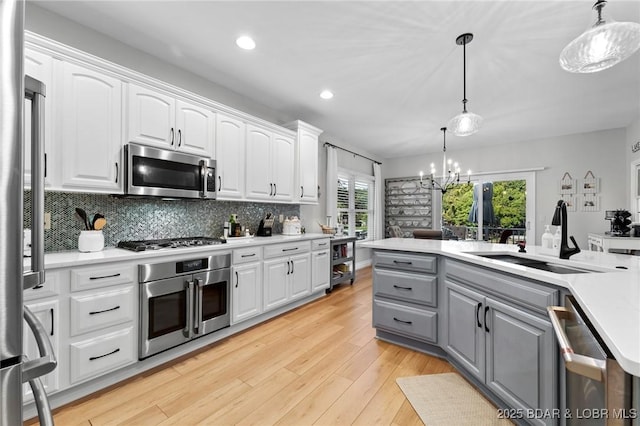 kitchen with white cabinets, sink, stainless steel appliances, and hanging light fixtures