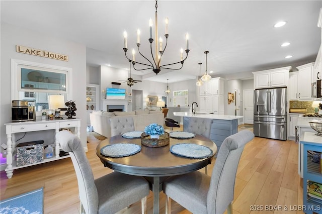 dining space with sink, light hardwood / wood-style floors, and ceiling fan with notable chandelier