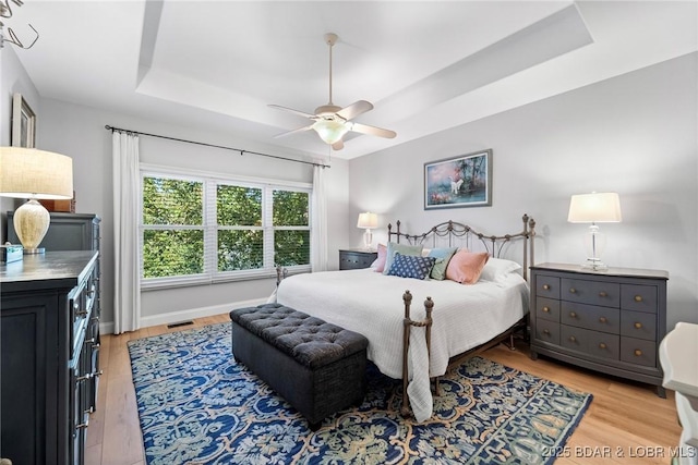 bedroom featuring a tray ceiling, light hardwood / wood-style flooring, and ceiling fan