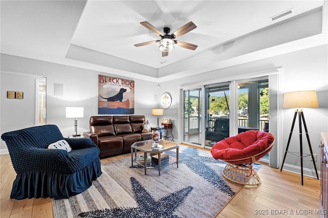 living room featuring a raised ceiling, ceiling fan, and light wood-type flooring