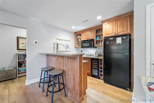 kitchen featuring a kitchen bar, sink, black appliances, light hardwood / wood-style floors, and wine cooler