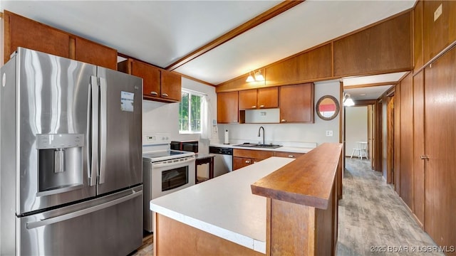 kitchen with appliances with stainless steel finishes, vaulted ceiling, sink, light hardwood / wood-style flooring, and a center island