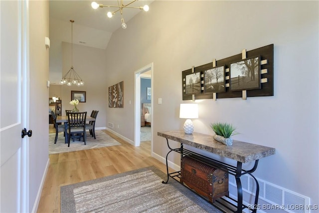 hall with hardwood / wood-style flooring, high vaulted ceiling, and a chandelier