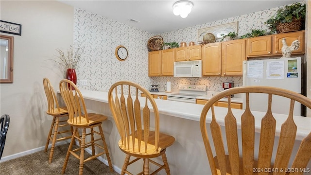 kitchen with a kitchen breakfast bar, light brown cabinetry, dark carpet, and white appliances