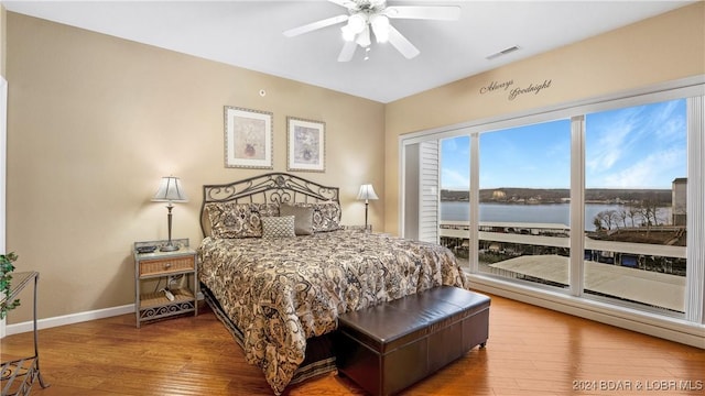 bedroom with hardwood / wood-style floors, a water view, and ceiling fan