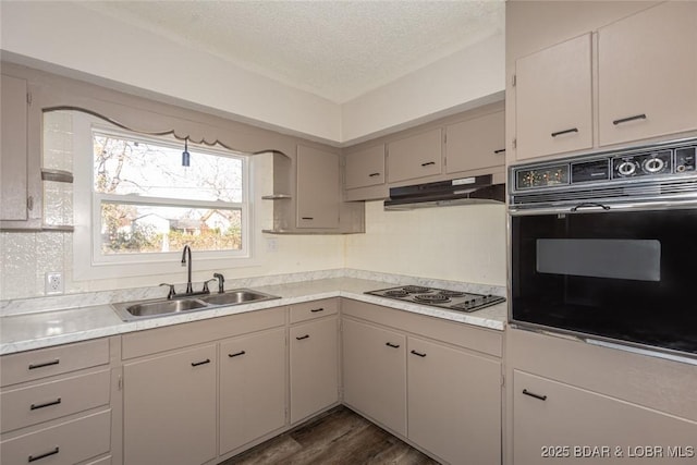 kitchen with a textured ceiling, dark wood-type flooring, sink, black oven, and stainless steel gas stovetop