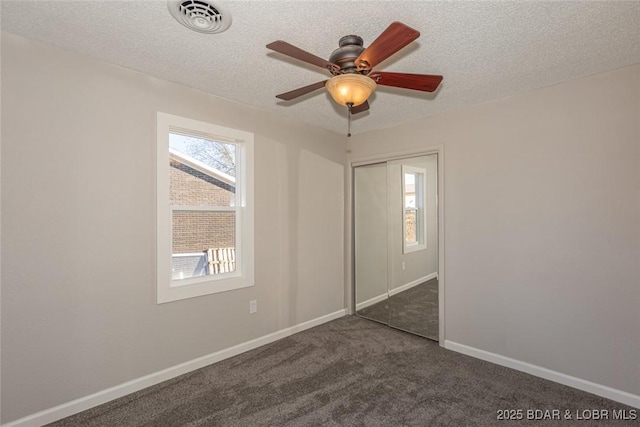 unfurnished bedroom with dark colored carpet, ceiling fan, a textured ceiling, and a closet