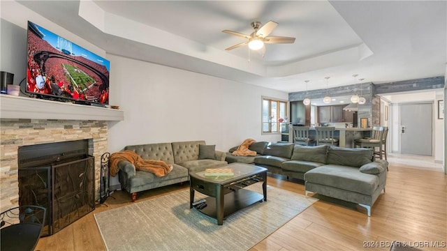 living room featuring ceiling fan, light hardwood / wood-style floors, a raised ceiling, and a fireplace