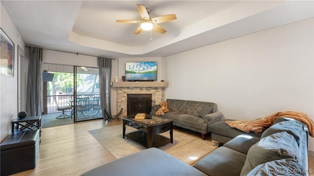 living room featuring a raised ceiling, ceiling fan, a fireplace, and light hardwood / wood-style floors