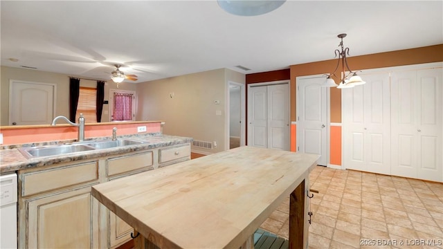 kitchen featuring ceiling fan with notable chandelier, white dishwasher, sink, decorative light fixtures, and a center island