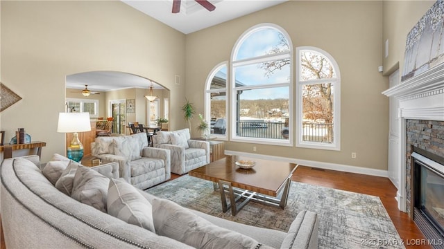 living room with a high ceiling, wood-type flooring, ceiling fan, and a fireplace