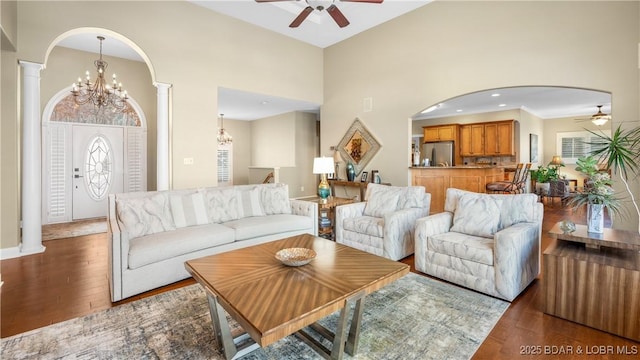 living room featuring ornate columns, hardwood / wood-style flooring, ceiling fan with notable chandelier, and a towering ceiling