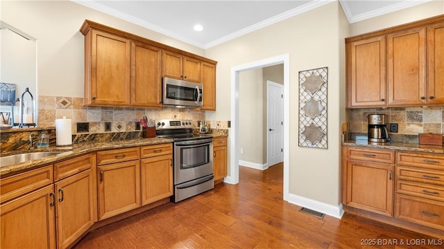 kitchen featuring dark wood-type flooring, ornamental molding, appliances with stainless steel finishes, and dark stone counters