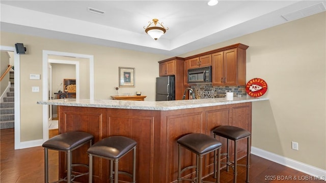 kitchen featuring a breakfast bar area, tasteful backsplash, refrigerator, a raised ceiling, and kitchen peninsula