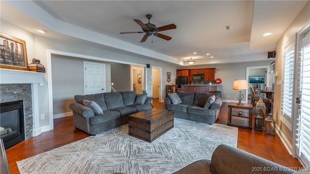 living room with ceiling fan, a tray ceiling, and dark hardwood / wood-style floors