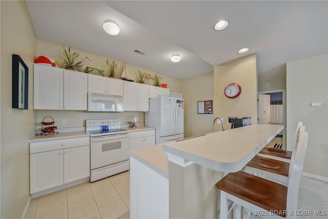 kitchen with white cabinetry, white appliances, a breakfast bar area, and light tile patterned floors