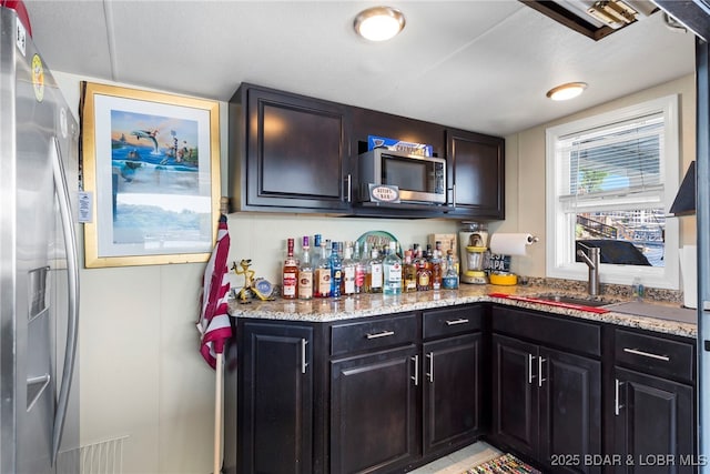 kitchen with dark brown cabinets, stainless steel appliances, light stone counters, and sink