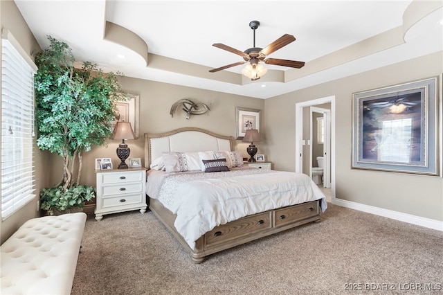 carpeted bedroom featuring a tray ceiling, ceiling fan, and ensuite bathroom