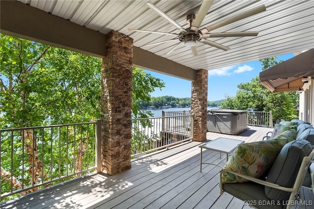 deck featuring ceiling fan, a water view, and a hot tub