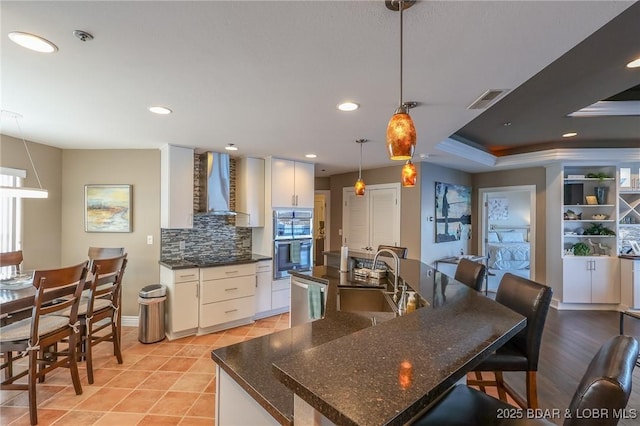 kitchen with white cabinetry, sink, wall chimney exhaust hood, decorative light fixtures, and appliances with stainless steel finishes