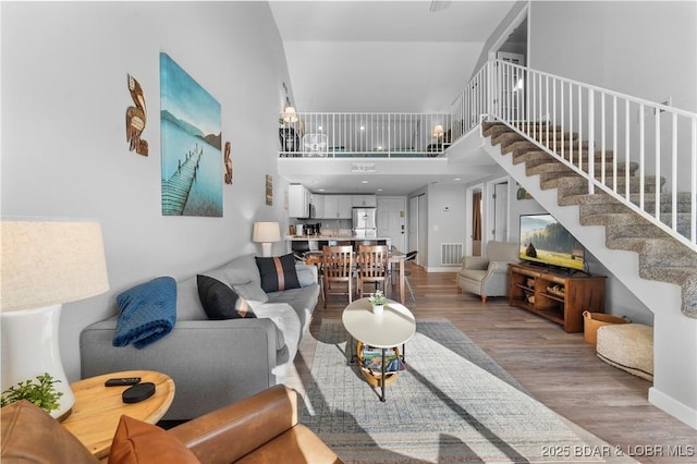 living room featuring visible vents, stairway, a towering ceiling, and wood finished floors