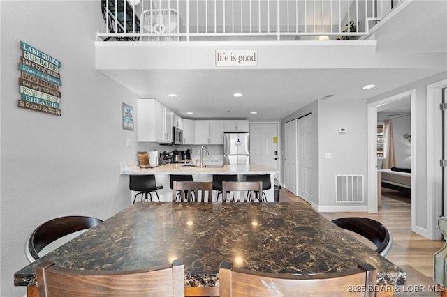 dining area featuring light wood-type flooring, visible vents, a towering ceiling, and baseboards