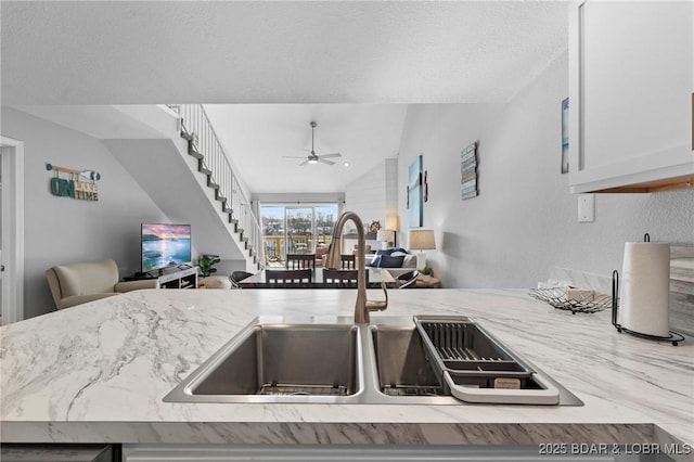 kitchen with lofted ceiling, light stone counters, a sink, a ceiling fan, and open floor plan