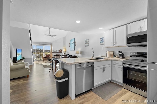 kitchen with appliances with stainless steel finishes, open floor plan, a sink, and a peninsula