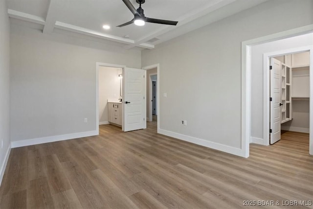 unfurnished bedroom with ensuite bathroom, a spacious closet, beam ceiling, and light hardwood / wood-style flooring