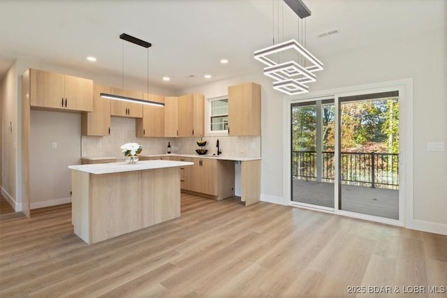 kitchen featuring hanging light fixtures, a kitchen island, light brown cabinetry, decorative backsplash, and light wood-type flooring