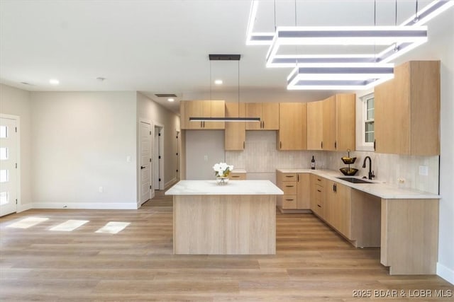 kitchen with sink, light brown cabinets, decorative light fixtures, a center island, and light hardwood / wood-style floors