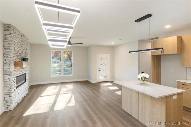 kitchen with light brown cabinetry, hardwood / wood-style flooring, a kitchen island, pendant lighting, and a fireplace