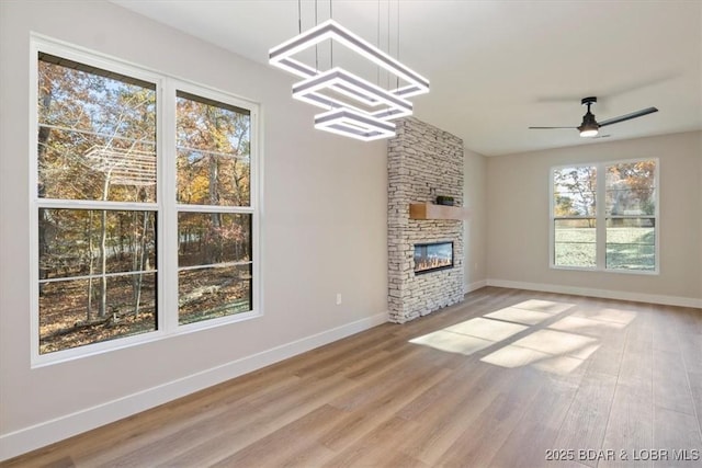 unfurnished living room with a stone fireplace, ceiling fan, and hardwood / wood-style flooring