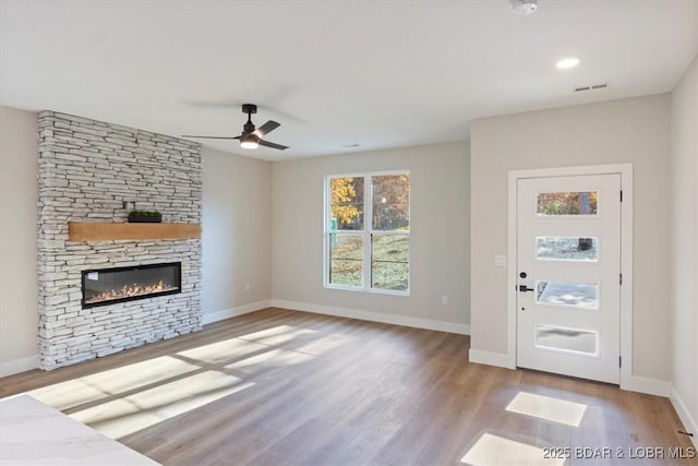 unfurnished living room featuring a stone fireplace, ceiling fan, and light hardwood / wood-style flooring