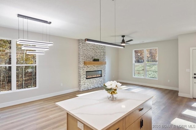 kitchen with hanging light fixtures, ceiling fan, light stone countertops, a fireplace, and a kitchen island